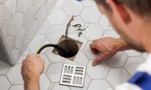 plumber unclogging blocked shower drain with hydro jetting at home bathroom. sewer cleaning service