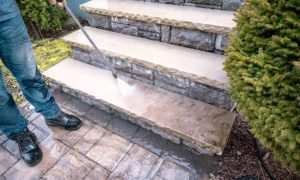 Man cleaning outdoor dirty porch stairs with a power wash machine.